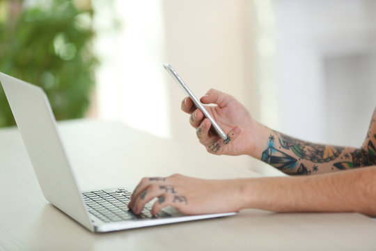 Young man with tattoo using laptop and mobile phone at the table