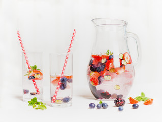 Summer drink with berries in jug and glasses with straw on white wooden background, side view