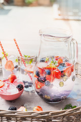 Pitcher with water, berries and  ice cubes on table over garden terrace background. Home scene with summer drinks.