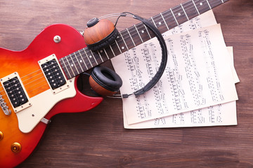 Naklejka premium Electric guitar with notes and headphones on wooden background
