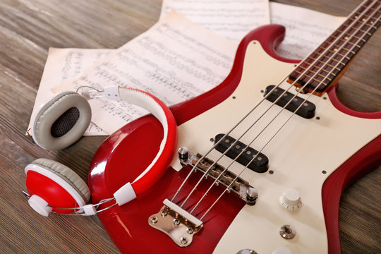 Electric guitar with headphones and notes on wooden background