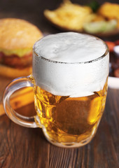 Glass mug of light beer with snacks on dark wooden table, close up