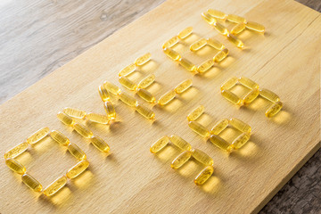 Omega 3-6-9 fish oil yellow softgels drawing omega 3-6-9  letters on wooden board on rustic table.