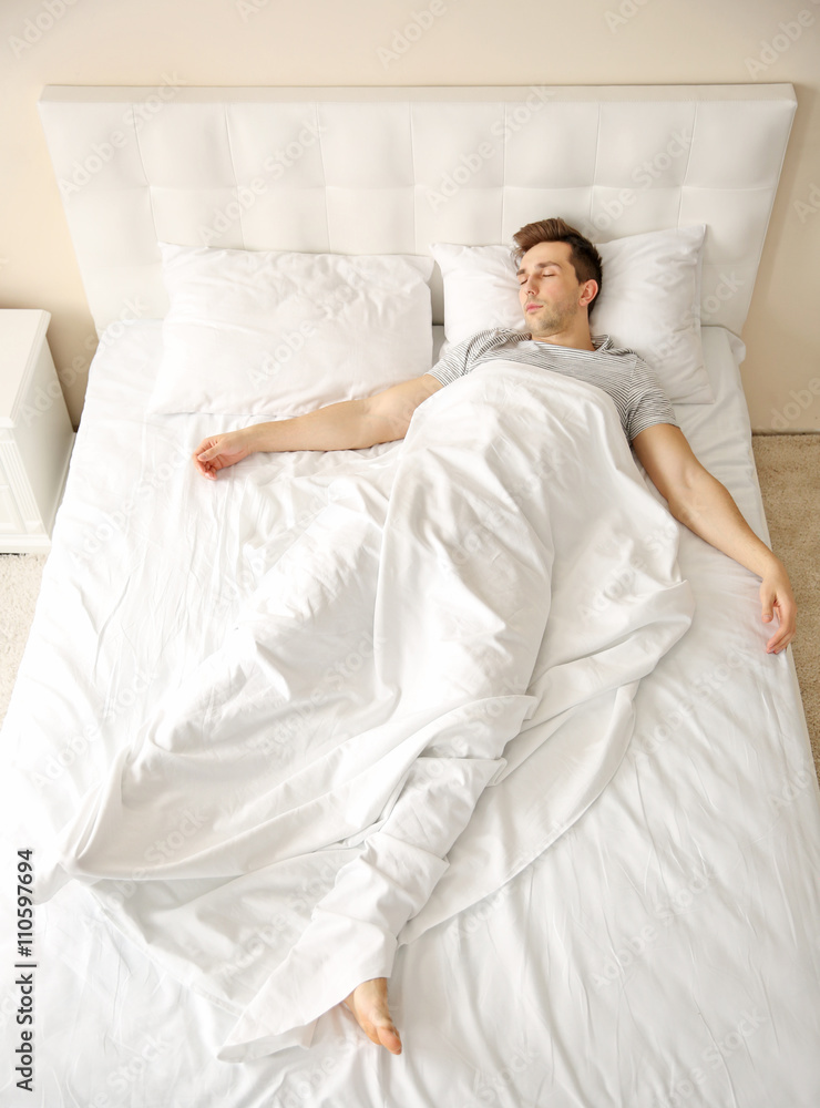 Wall mural Young man sleeping alone in white big bed