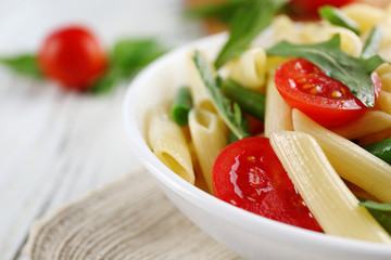 Boiled penne pasta with tomatoes, French bean and arugula on white plate
