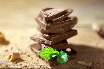 Stack of black chocolate pieces with fresh mint on wooden table