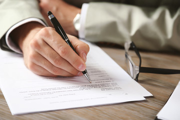 Male hand with pen signing document at the desk closeup