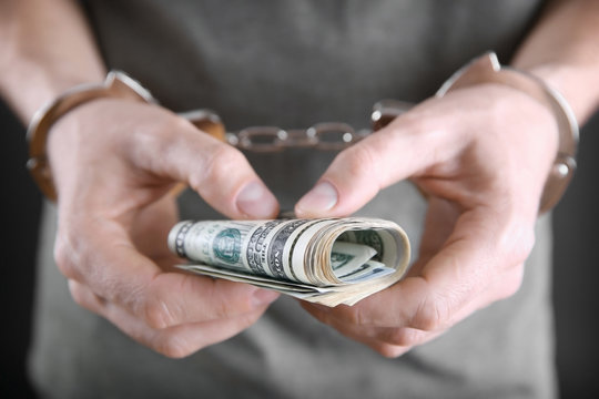 Man in handcuffs holding dollar banknotes, close up
