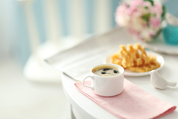 Cup of coffee with wafers on white table in light interior