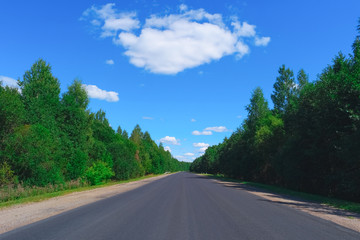 Empty highway, green forest and clouds