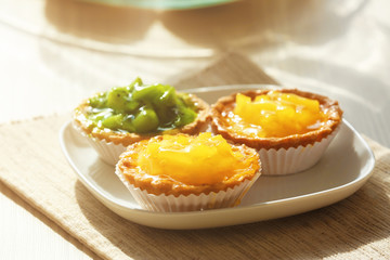 Fresh homemade fruit tarts with citruses and kiwi on a white table.