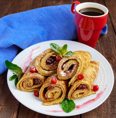 Golden pancakes in the form of roll with strawberry jam and powdered sugar on a white plate on a wooden table. Close-up. Breakfast