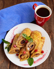Golden pancakes in the form of roll with strawberry jam and powdered sugar on a white plate on a wooden table. Breakfast