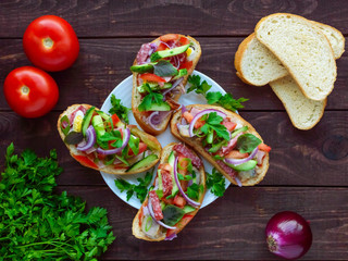 Sandwiches with greens, tomatoes, meat, salami on crispy bread on the table. The top view