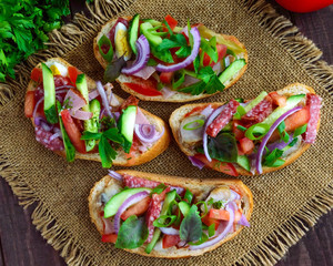 Sandwiches with greens, tomatoes, meat, salami on crispy bread on the table