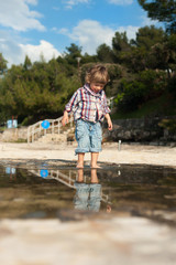 Cute little boy on the beach having fun playing and jumping in a puddle of seawater. Reflection in a water.