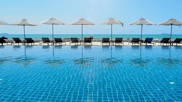 Umbrella and swimming pool in hotel resort with sea beach background.
