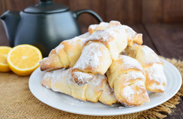 Sweet homemade lemon croissants with powdered sugar. Teapot