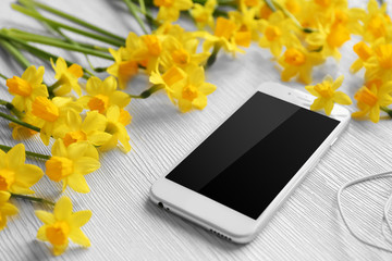 Fresh narcissus flowers with mobile phone and earphones on wooden background