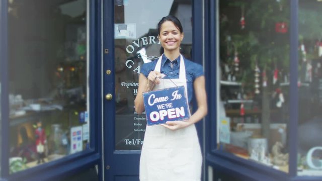  Happy female shopkeeper holds up a sign to show she is open for business