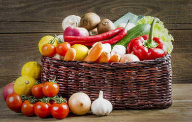 Wicker basket with fruits and vegetables on wooden table