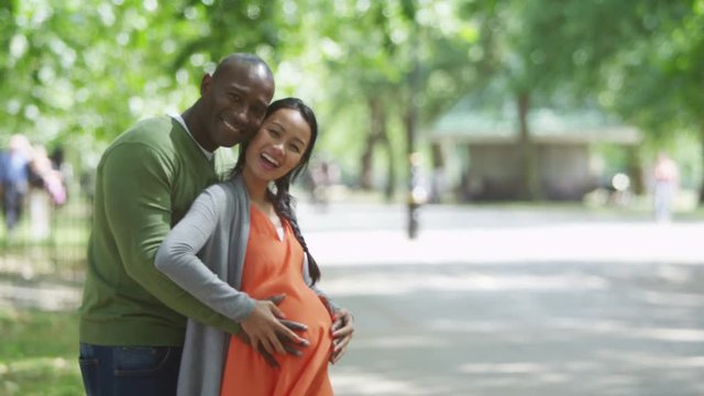  Portrait of happy pregnant couple relaxing in the park with hands on tummy