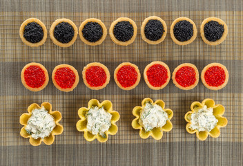 Obraz na płótnie Canvas Tartlets filled with cheese and dill salad and caviar on bamboo placemat