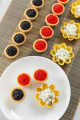 Tartlets filled with cheese and dill salad and caviar on bamboo placemat and plate with tartlets