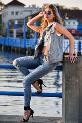 Young fashion model dressed in ripped jeans and vest posing pretty on the pier.