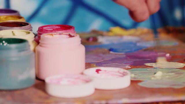 The artist mixes paint on the palette. In the foreground, a jar of paint