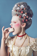 Young woman greedy eating marshmallow in light corset over blue background. Updo baroque hairstyle...