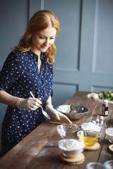 Young woman prepares bath bombs. Ingredients and floral decor on a wooden vintage table.