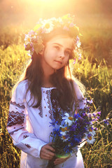 portrait of little girl in a field with a bouquet of wild flowers and a wreath on her head dreamily...