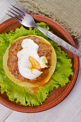 Beef and pork patty with poached egg, smashed potato and lettuce. View from above, top studio shot