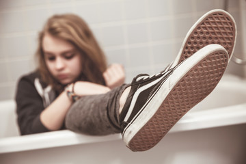 Teenage girl in black sneakers sits in bath