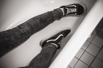 Teenager in black sneakers lays in white bath