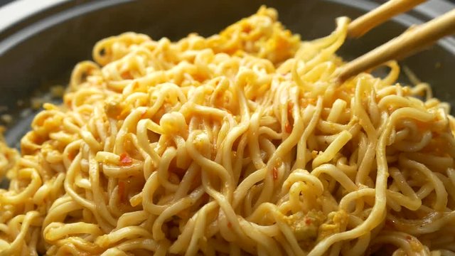 close up of chopsticks stirring cooking instant noodles in frying pan
