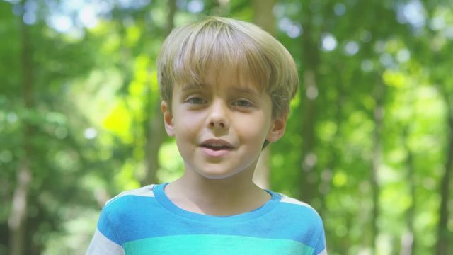  Portrait of happy little boy in the woods, waving & talking to camera