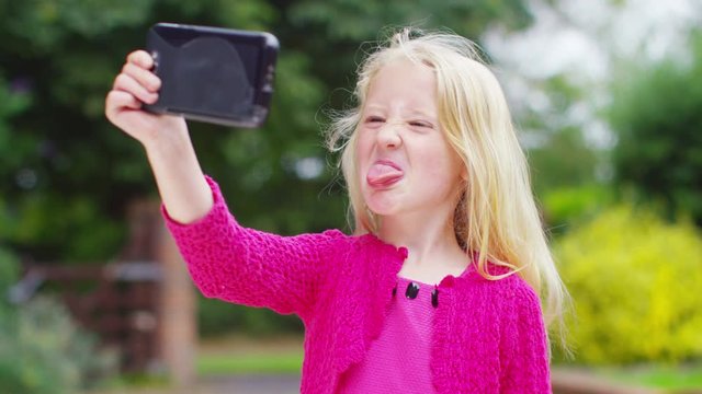  Happy little girl looking at computer tablet and pulling faces outdoors
