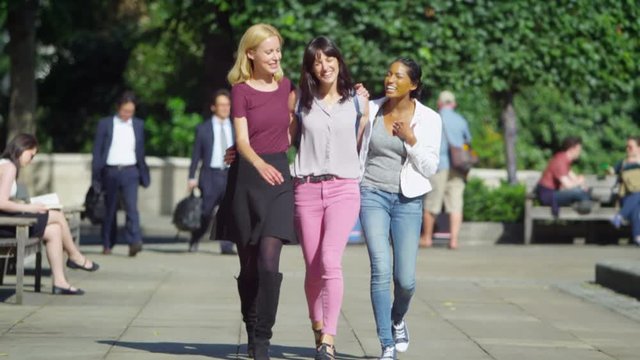  Happy attractive female friends chatting as they walk through city