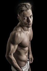 Lean athletic shirtless young man standing on dark background