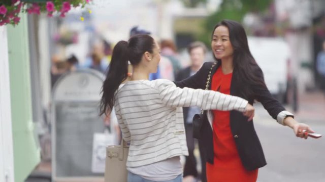  Attractive female friends meet up and greet each other outdoors in the city. 
