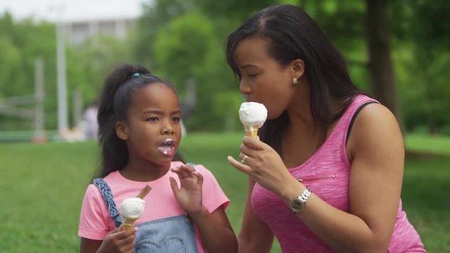  African American mother & daughter eating ice cream in the park together. 