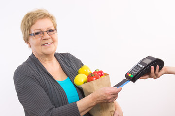 Senior woman holding shopping bag and using payment terminal with credit card, cashless paying for shopping