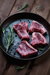 Close-up of a frying pan with raw seasoned T-bone lamb steaks