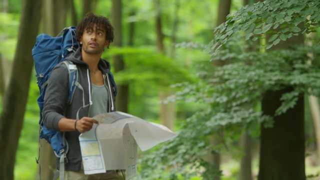  Man hiking in the woods on his own, looking at map and trying to find his way. 