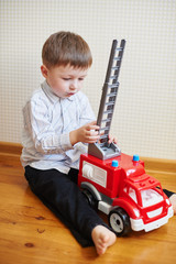 little boy playing red toy machine in room