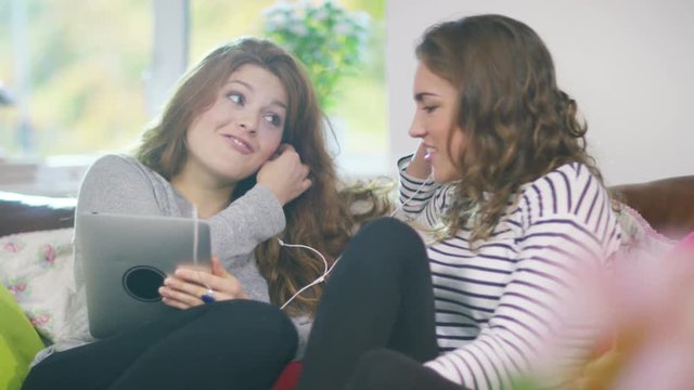  Young female friends listening to music with earphones & computer tablet
