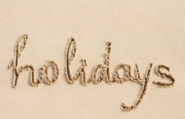 Word Holidays handwritten on sand