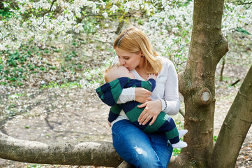 Naklejka premium mother with her baby son sitting on tree branch in spring garden